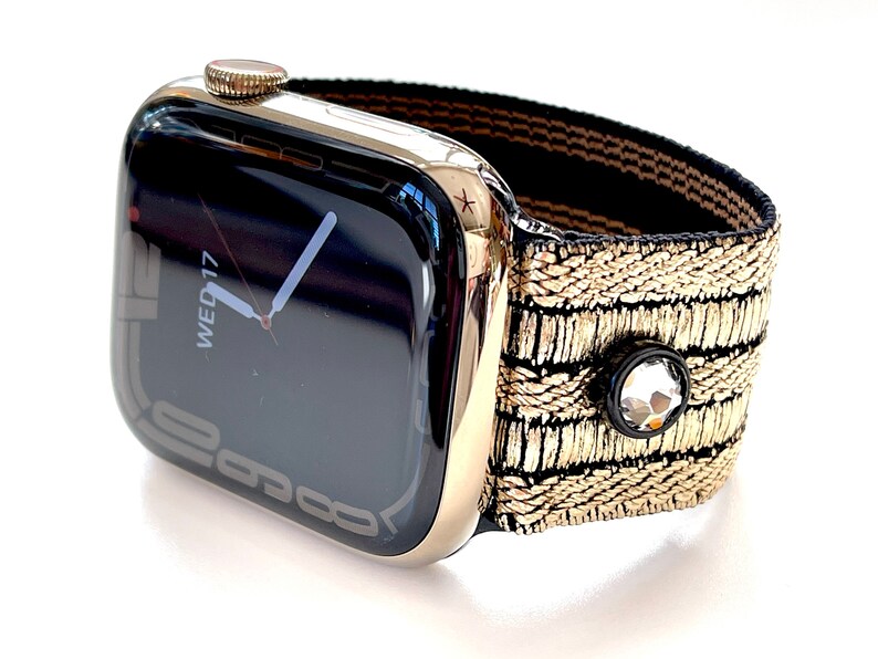 May include: A gold Apple Watch with a black and gold patterned band. The watch face displays the date and time, showing "WED 17".