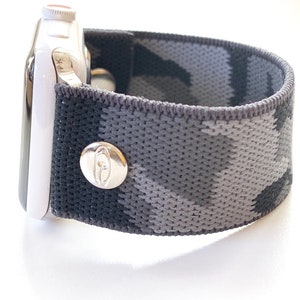 May include: A black and grey camouflage patterned elastic Apple Watch band with a silver buckle.