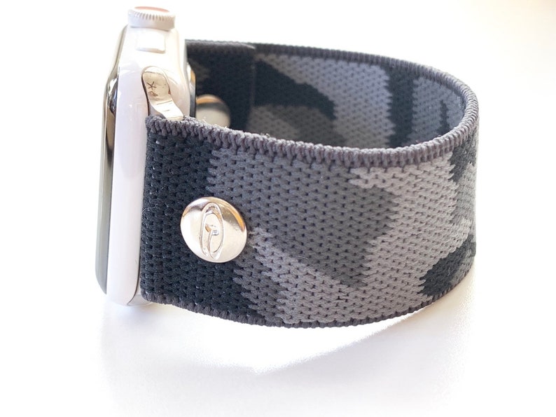 May include: A black and grey camouflage patterned elastic Apple Watch band with a silver buckle.