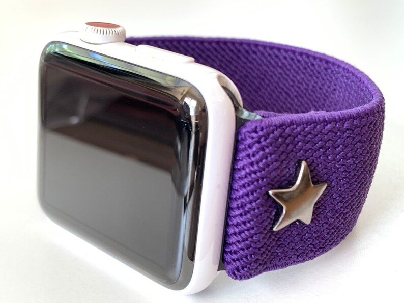 May include: A white Apple Watch with a purple elastic band and a silver star charm.