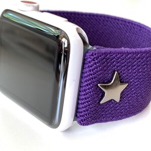 May include: A white Apple Watch with a purple elastic band and a silver star charm.