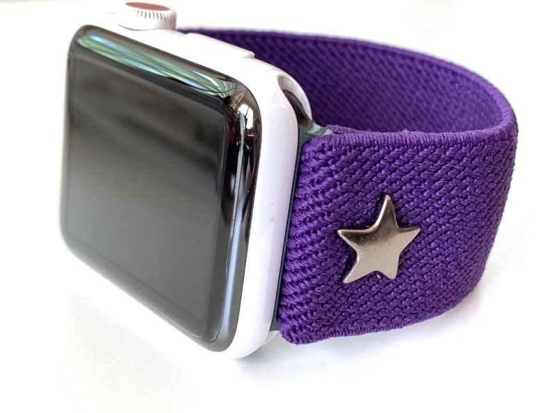 May include: A white Apple Watch with a purple elastic band and a silver star charm.