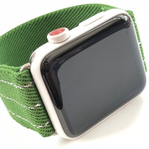 Puede incluir: Un Apple Watch plateado con una banda deportiva de rayas verdes y blancas. La esfera del reloj es negra y la corona digital es roja.