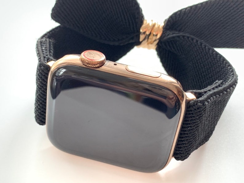 May include: A rose gold Apple Watch with a black woven band. The watch face is black and the band is made of a soft, stretchy material.