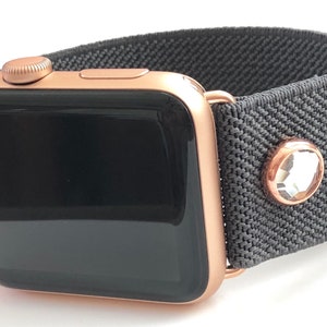 May include: A rose gold Apple Watch with a gray fabric band and a clear crystal embellishment.