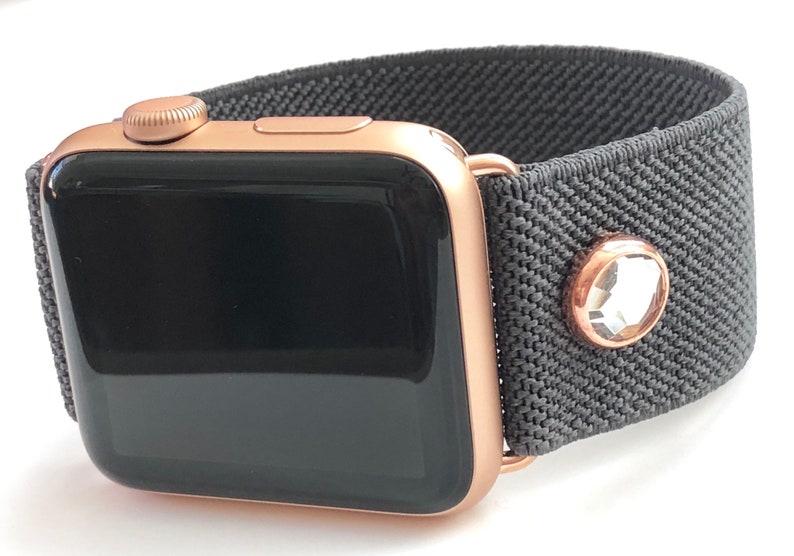 May include: A rose gold Apple Watch with a gray fabric band and a clear crystal embellishment.
