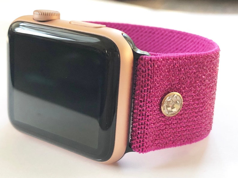 May include: A rose gold Apple Watch with a pink sparkly sport band. The band has a small rhinestone embellishment.