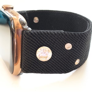 May include: A black watch band with rhinestones. The band is made of a stretchy fabric and has a rose gold watch attached.