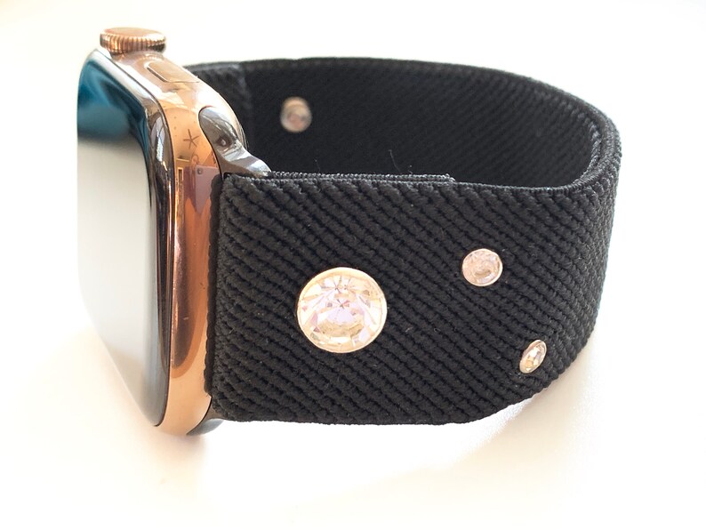 May include: A black watch band with rhinestones. The band is made of a stretchy fabric and has a rose gold watch attached.