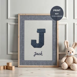 Puede incluir: Un cuadro con la letra "J" azul marino y el nombre "Jack" debajo. La impresión tiene un fondo blanco, un borde de tela azul y un marco de madera. Un conejo de peluche y bloques de madera en primer plano, para una habitación infantil.