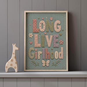 Puede incluir: Un cuadro decorativo con el texto LONG LIVE Girlhood en estilo patchwork con bordados de flores y mariposas sobre un fondo verde salvia, acompa&ntilde;ado de una figura de jirafa de madera de color claro situada a la izquierda.