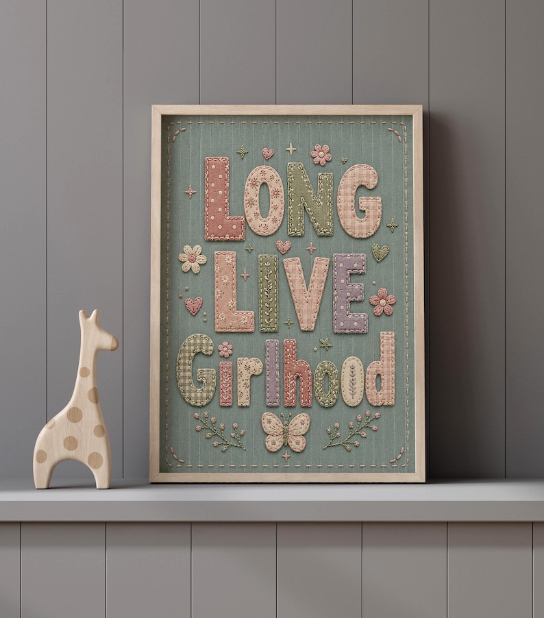 Puede incluir: Un cuadro decorativo con el texto LONG LIVE Girlhood en estilo patchwork con bordados de flores y mariposas sobre un fondo verde salvia, acompa&ntilde;ado de una figura de jirafa de madera de color claro situada a la izquierda.
