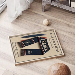 May include: A framed rectangular print featuring a navy blue scarf with red and white stripes, a fleur-de-lis emblem, and the text "FRANCE", "FAIT POUR R&Ecirc;VER", "CON&Ccedil;U POUR L'&Eacute;QUIPE", "PASSION. FIERT&Eacute;. FRANCE.", and "DEPUIS 1919" on a beige background.