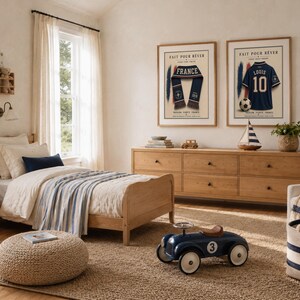 May include: A bedroom featuring a light wood bed frame with cream bedding and a blue striped throw, a matching six-drawer dresser, and two framed prints on the wall. One print shows a blue scarf, the other a blue jersey with the text FAIT POUR R&Ecirc;VER.
