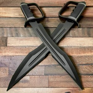 May include: Two black swords with a grey stripe design are crossed against a wooden background. Each sword has a handle with a D-shaped guard and a decorative silver band. The blades are long and pointed.