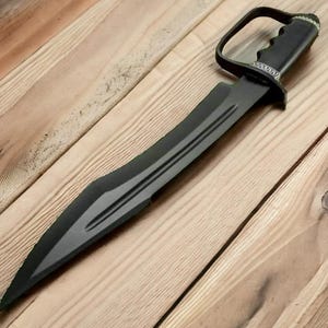 May include: A black sword with a curved blade and a handle with a finger loop. The blade has a central fuller and a pointed tip. The handle is textured for grip and has a decorative silver-coloured trim.