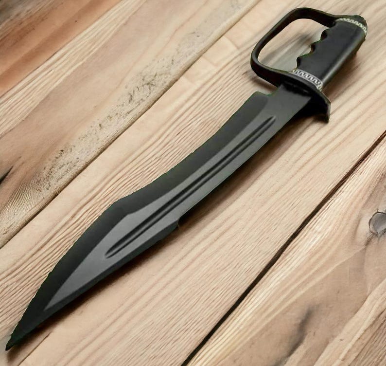 May include: A black sword with a curved blade and a handle with a finger loop. The blade has a central fuller and a pointed tip. The handle is textured for grip and has a decorative silver-coloured trim.