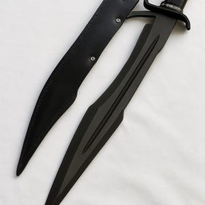 May include: A black sword with a curved blade and a handle with a guard. The sword is accompanied by a black leather sheath. The handle has a grip for a secure hold. The sword is likely made of metal.