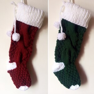 May include: Two knitted Christmas stockings. One is burgundy with a white cuff, toe, and pom-poms. The other is green with a white cuff, toe, and pom-poms. Both stockings have a cable knit design.