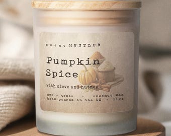 May include: A frosted glass candle jar with a light wood lid. The label reads SCENT HUSTLER, Pumpkin Spice with clove and nutmeg, non-toxic, coconut wax, hand poured in the US, 11oz. The label features an illustration of a pumpkin and spices.