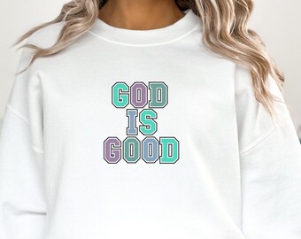 May include: White sweatshirt with a graphic print that says "GOD IS GOOD" in colorful block letters.