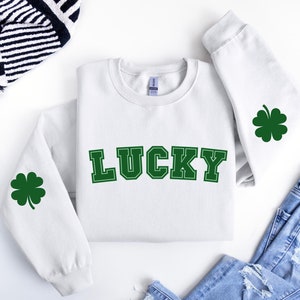 May include: White sweatshirt with green shamrock designs on the sleeves and the word "LUCKY" in green block letters on the front.