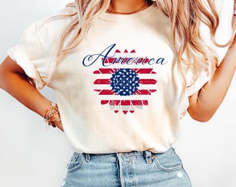 May include: A white t-shirt with a distressed American flag sunflower design and the word "America" in a cursive font.