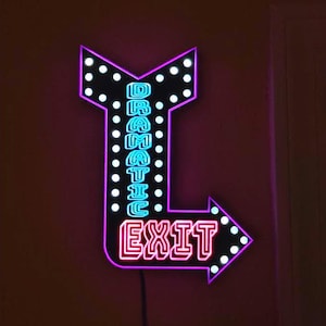 May include: A neon sign in the shape of an arrow, with the word "EXIT" in bright pink and the word "DRAMATIC" in blue. The sign has a black background with white dot accents and a purple outline.