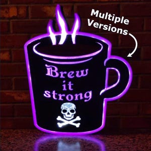 May include: A black coffee mug-shaped sign with a purple neon outline and accents. The text "Brew it strong" is displayed, along with a skull and crossbones. The sign is illuminated, creating a glowing effect.