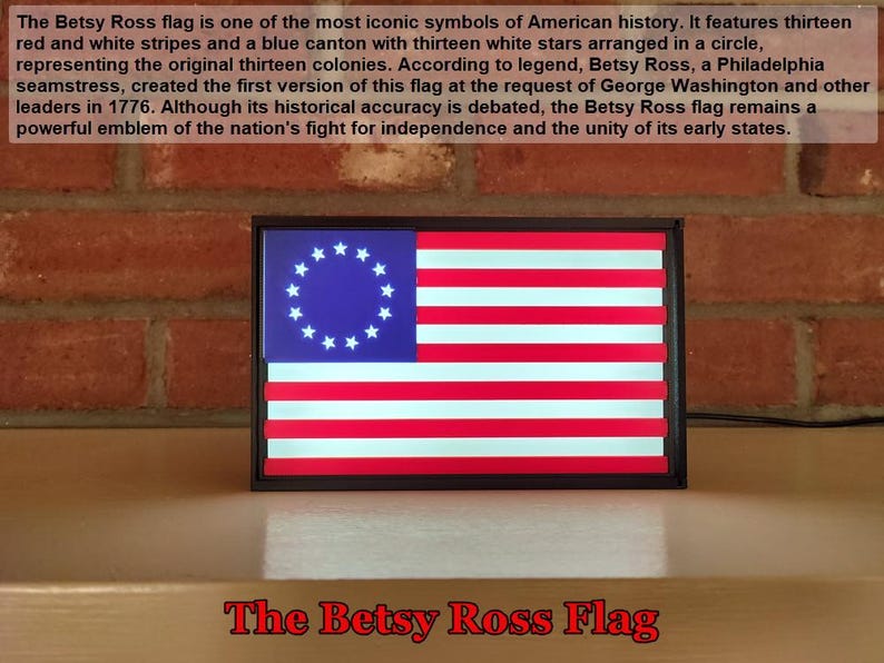 May include: A framed replica of the Betsy Ross flag, a historical American flag with thirteen red and white stripes and a blue canton with thirteen white stars arranged in a circle. The frame is black and the flag is illuminated. The text "The Betsy Ross Flag" is printed below the frame.