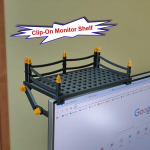 May include: A black and gold clip-on monitor shelf with a fence-like design and a grid-patterned surface. The shelf features four corner posts with gold finials and is attached to the top edge of a computer monitor. Text reads Clip-On Monitor Shelf.