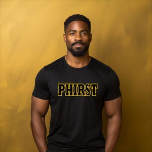 May include: Black t-shirt with the word "PHIRST" in gold block letters with a yellow outline. The text is centered on the chest. The background is a solid gold color.