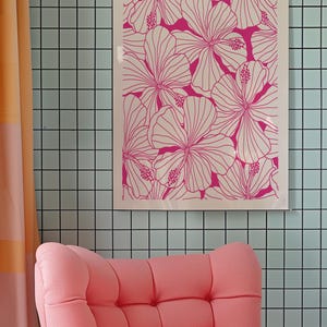 May include: A pink armchair with a tufted back and seat sits in front of a wall with a framed print of pink hibiscus flowers on a white background.