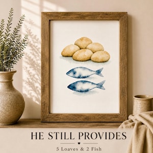 Puede incluir: Impresión en acuarela enmarcada que representa seis panes dorados sobre dos peces azules. El texto "HE STILL PROVIDES" y "5 Loaves & 2 Fish" está en la parte inferior. La obra de arte se exhibe en una estantería de madera.