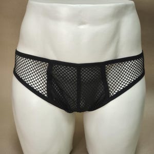 Puede incluir: Ropa interior de malla negra con un panel frontal negro liso y una cintura de malla. La ropa interior se muestra en un maniquí blanco.