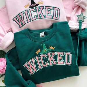 May include: Two sweatshirts with the word "WICKED" in pink letters with a witch's hat and crown graphic. One sweatshirt is pink and the other is green.