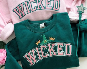 May include: Two sweatshirts with the word "WICKED" in pink letters with a witch's hat and crown graphic. One sweatshirt is pink and the other is green.