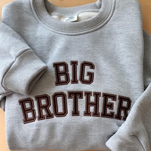May include: Gray sweatshirt with brown embroidered text that reads "BIG BROTHER".