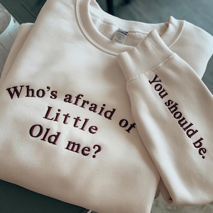 May include: A cream colored sweatshirt with the text "Who's afraid of little old me?" embroidered in maroon on the front and "You should be." embroidered in maroon on the sleeve.