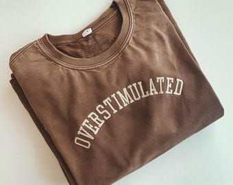May include: A brown t-shirt with the text "OVERStimulated" in white embroidery.