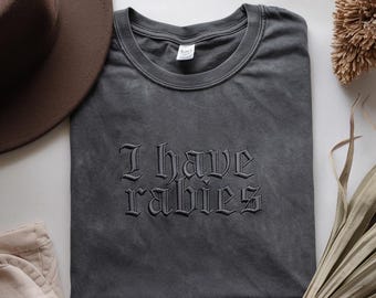 May include: A dark gray t-shirt with the text "I have rabies" embroidered in black gothic lettering.