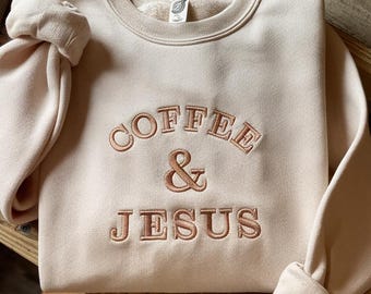 Op de afbeelding: Een beige sweatshirt met de tekst "COFFEE & JESUS" geborduurd in bruin op de voorkant.