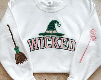 May include: White sweatshirt with a green witch hat, pink and green "WICKED" text, and a brown broom and pink wand embroidered on the sleeves.