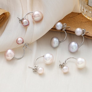 May include: A set of six pairs of pearl earrings. Each earring features two pearls, one larger than the other, connected by a curved silver bar. The pearls are in shades of white, pink, and grey.