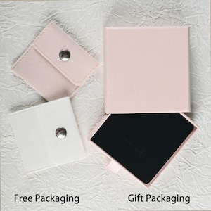 May include: Overhead view of jewellery packaging options. Two small pouches, one white and one pink, each with a silver snap closure. A pink square box is open, revealing a black interior. Text reads "Free Packaging" and "Gift Packaging."