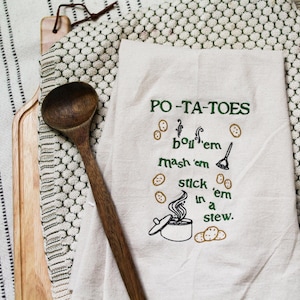 May include: A white kitchen towel with green embroidery that reads "PO-TA-TOES boil 'em mash 'em stick 'em in a stew."