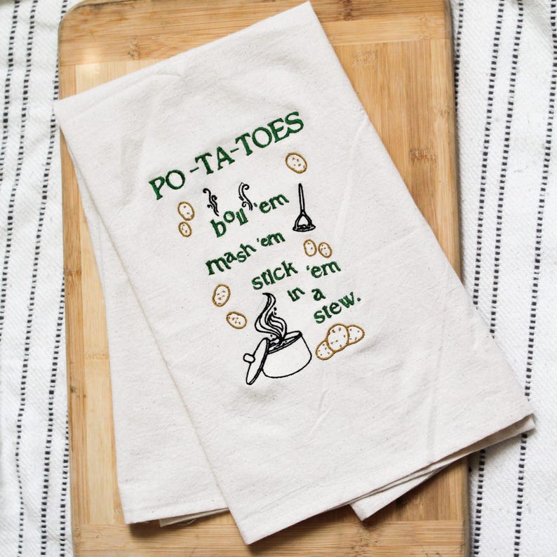 An unbleached off white linen tea towel embroidered with a quote from Lord of the Rings movie, the Two Towers. The Quote is Potatoes. Boil 'em, mash 'em, stick'em in a stew. Playful potatoes fall down to a  large whimsical pot, and a classic potatoes masher. The fonts represent the verbs, with steam coming off of the boil em phrase and the letters in mashed closely pushed together. Colors are a bold emerald green and a soft golden brown. Hang this towel in kitchen of any hobbit, elf, or wizard.