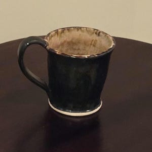 May include: A dark blue ceramic mug with a light brown rim and a white base. The mug has a rounded shape and a handle.
