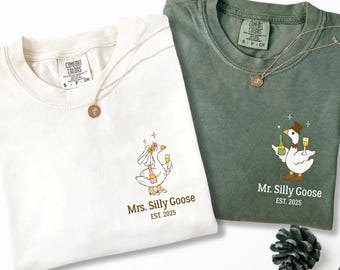 May include: Two t-shirts, one white and one green, with matching gold necklaces. The white shirt features a goose bride graphic with the text "Mrs. Silly Goose EST. 2025." The green shirt has a goose groom graphic with the text "Mr. Silly Goose EST. 2025."