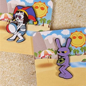 Puede incluir: Dos pines de esmalte con personajes de dibujos animados en tarjetas con temática de playa. Un pin representa a un personaje con un gorro de bufón sosteniendo un balón de playa. El otro pin muestra un conejo morado sosteniendo una tortuga verde.